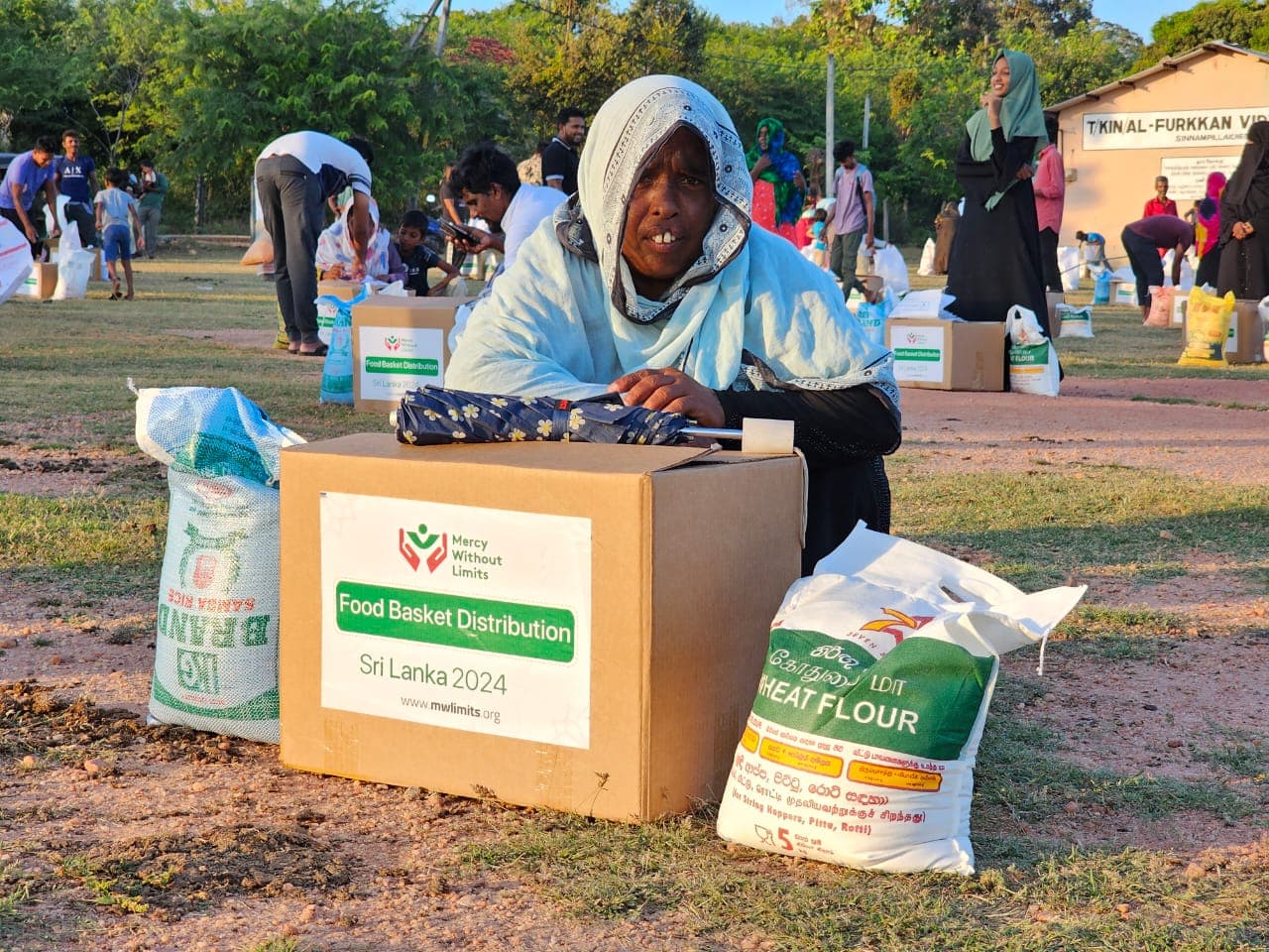 A woman smiling beside her food basket at a distribution in Sri Lanka.