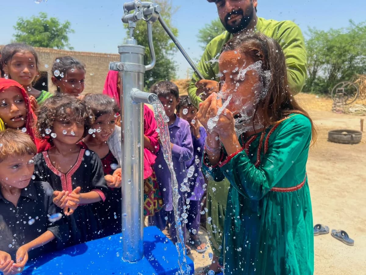 Children drinking and playing with water at SDQA's completed water pump in Sindh.