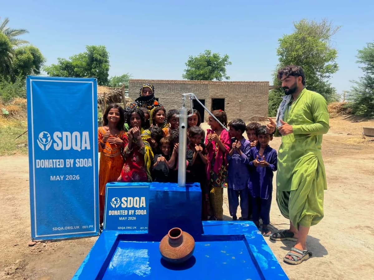 Children and adults gathered beside SDQA's completed blue water pump in Sindh.